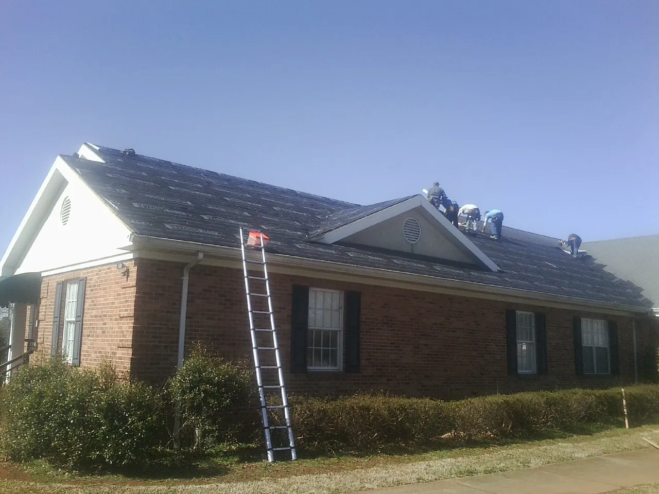 Crew tearing shingles off a brick ranch roof with a ladder set — Metal Roof Repair work by our crew in Danville