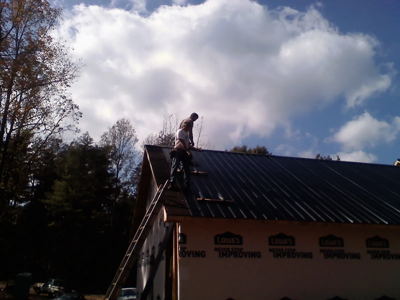 Roofer fastening dark metal panels high against a cloudy sky, from a Roof Inspection job in Danville